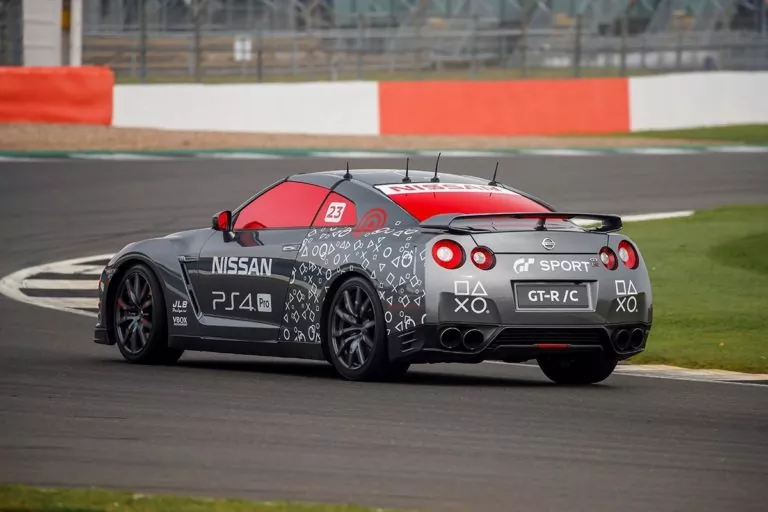 Ein maßgeschneiderter Nissan GT-R mit PlayStation- und Gran Turismo-Branding fährt auf einer Rennstrecke. Der Nissan GT-R trägt Aufkleber mit PlayStation-Symbolen, rot getönte Scheiben und ein unverwechselbares GT Sport-Kennzeichen.