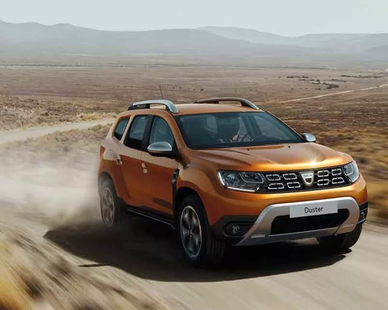 Ein orangefarbener Dacia Duster SUV fährt auf einem staubigen Feldweg durch eine trockene, offene Landschaft mit Hügeln im Hintergrund unter einem klaren Himmel - perfekt, um Fahrzeuge der Auto Mattern Servicewerkstatt zu testen, egal ob Neuwagen oder Gebrauchtwagen.