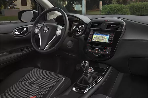 Innenansicht eines modernen Fahrzeugs mit Lenkrad, Armaturenbrett mit Touchscreen-Navigationssystem, Bedientasten, manueller Schaltung und Vordersitzen mit gemusterter Polsterung.