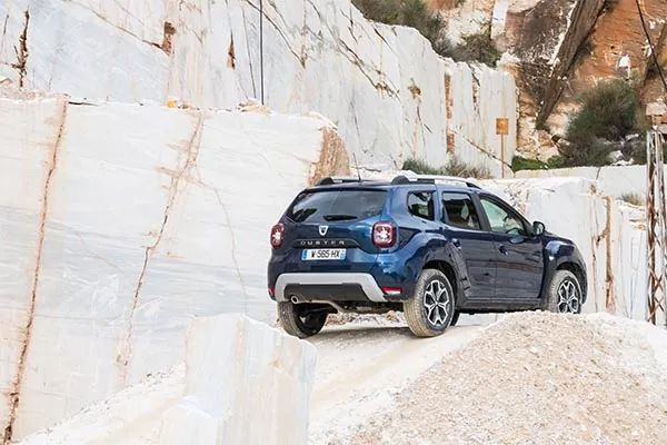 Ein blauer Geländewagen fährt auf einem felsigen, unebenen Weg, umgeben von hohen, weißen Steinfelsen in einem Steinbruch.
