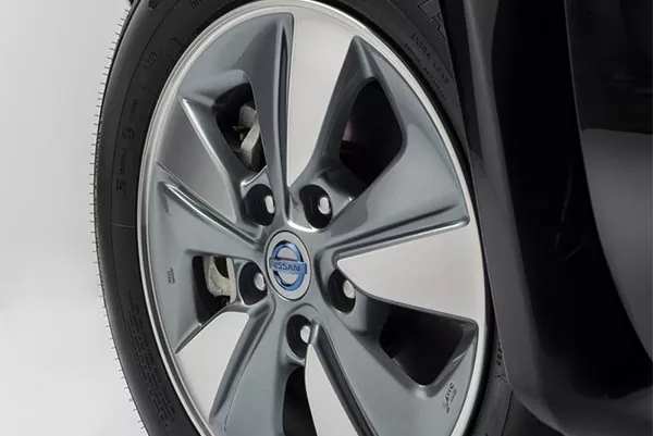 Nahaufnahme eines silbernen Leichtmetallrads mit einem blauen Nissan-Logo in der Mitte, das an einem schwarzen Auto angebracht ist. Das Reifenprofil und ein Teil der Fahrzeugkarosserie sind ebenfalls zu sehen.