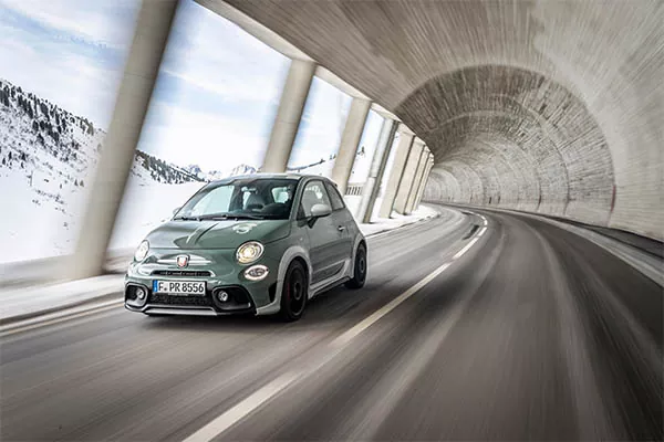 Ein kleines, sportliches Auto fährt durch einen geschwungenen Bergtunnel mit schneebedeckten Gipfeln, die ein Gefühl von Geschwindigkeit und Bewegung vermitteln.