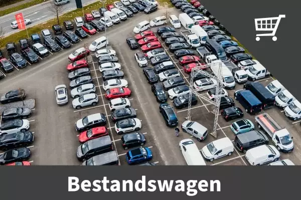 Luftaufnahme eines großen Parkplatzes mit vielen geparkten Fahrzeugen. Das Bild hat eine graue Überlagerung mit einem Einkaufswagen-Symbol und dem Wort Bestandswagen darunter, was die große Auswahl an Gebrauchtwagen bei Auto Mattern hervorhebt.