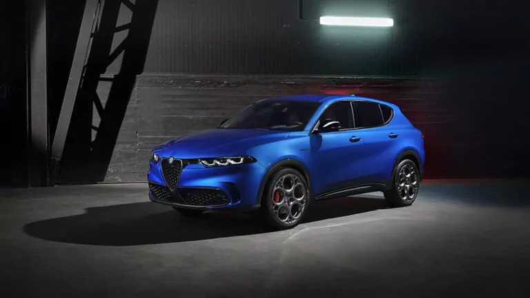 Ein blauer Alfa Romeo Tonale Geländewagen mit schnittigem, modernem Design und sportlichen Rädern ist in einem Innenraum vor einer dunklen Industriewand geparkt und wird von einer Deckenbeleuchtung angestrahlt.