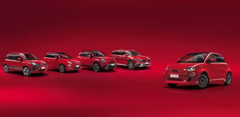 Fünf rote Fiat 500e Elektroautos werden in einer Reihe auf einer reflektierenden roten Fläche mit rotem Farbverlauf präsentiert. Vier Autos sind auf der linken Seite gruppiert, während auf der rechten Seite ein Auto allein steht.