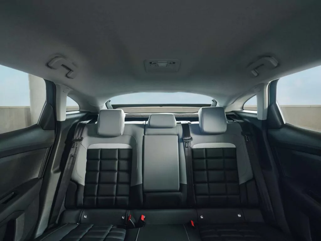 Blick von der Rückbank eines Autos, mit schwarzen Ledersitzen mit Steppmuster, drei Kopfstützen, Sicherheitsgurten und einer Heckscheibe, durch die Sonnenlicht einfällt.