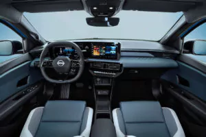 Modernes Fahrzeuginterieur mit digitalem Armaturenbrett, großem zentralen Touchscreen-Display, Multifunktionslenkrad und blaugrauen Sitzen mit hellen Akzenten, vom Rücksitz aus gesehen.