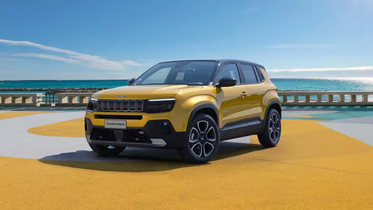 Ein gelber Jeep Avenger SUV ist auf einer leuchtend gelben und grauen Fläche in der Nähe einer Strandpromenade geparkt, mit dem Meer und dem blauen Himmel im Hintergrund - perfekt für ein Vorpremiere Jeep Avenger Preview Bielefeld Erlebnis.