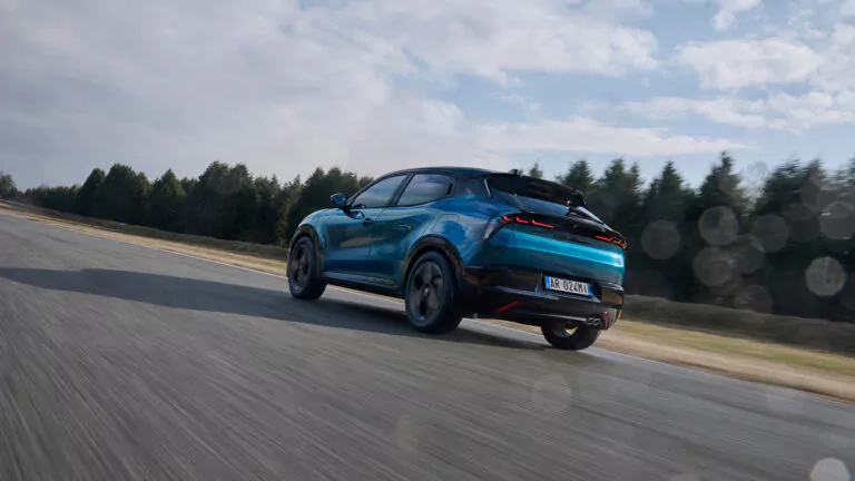 Ein blauer, sportlicher Geländewagen fährt schnell auf einer geraden, leeren, von Bäumen gesäumten Straße, über der ein teilweise bewölkter Himmel hängt. Das Foto wurde von hinten aufgenommen und fängt das Fahrzeug in Bewegung ein.