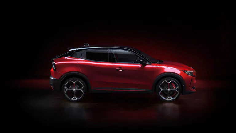 Ein schnittiger, roter Kompakt-SUV wird in der Profilansicht vor einem dunklen Hintergrund gezeigt, der sein modernes Design, die großen Leichtmetallräder und die sportlichen schwarzen Dachakzente hervorhebt.