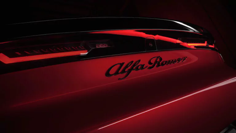 Nahaufnahme des Hecks eines roten Alfa Romeo mit dem beleuchteten Rücklicht und der "Alfa Romeo"-Plakette unter dramatischer roter und schwarzer Beleuchtung.