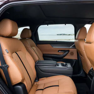 Der Innenraum eines Mazda CX-80 als Plug-in-Hybrid ist mit luxuriösen, hellbraunen Ledersitzen ausgestattet und bietet durch die Fenster einen atemberaubenden Blick auf das Meer. Die Rücksitze verfügen über eine Mittelarmlehne, und das Fahrzeug wirkt geräumig und modern – Entdecken Sie die Möglichkeiten.