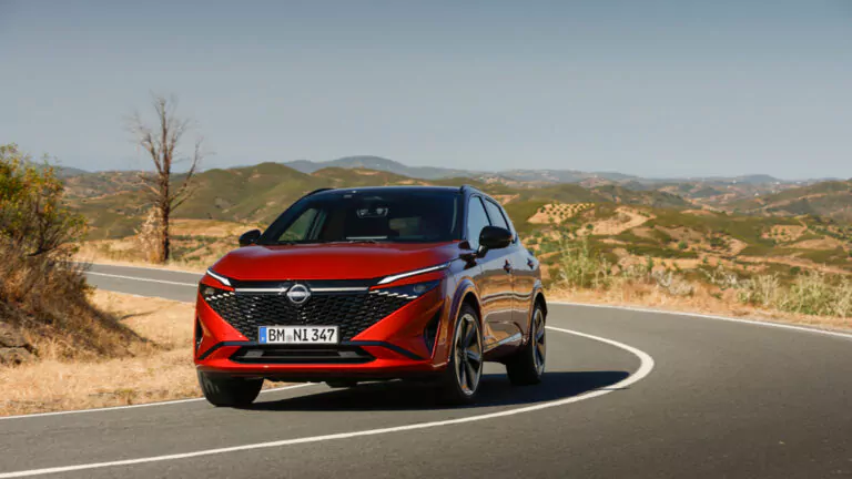 Ein roter Opel Geländewagen fährt auf einer kurvenreichen Straße durch eine trockene, hügelige Landschaft unter einem strahlend blauen Himmel.