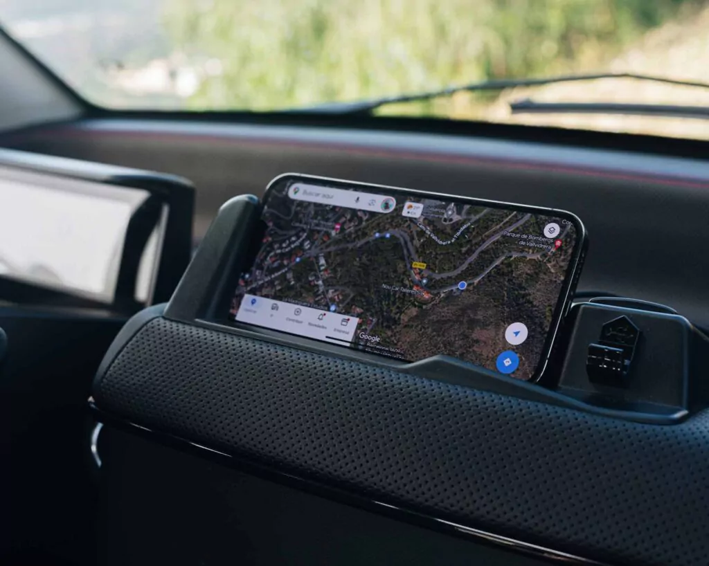 Auf dem Armaturenbrett eines Autos ist ein Smartphone mit einer Kartennavigations-App angebracht, die die ruhige Fahrt unterstreicht - perfekt für Erkundungen mit dem Nissan Silence Angebot, während im Hintergrund Bäume und Landschaft durch die Windschutzscheibe zu sehen sind.