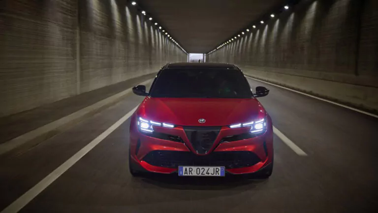 Ein roter Sportwagen mit hellen LED-Scheinwerfern fährt durch einen gut beleuchteten Tunnel, von vorne gesehen. Das Auto hat ein italienisches Nummernschild mit der Aufschrift AR 024 JR.