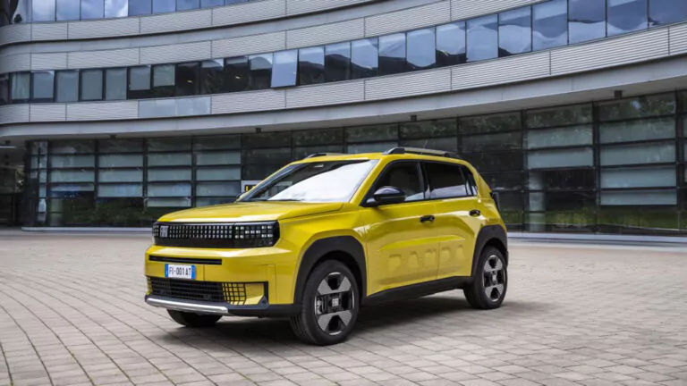 Ein leuchtend gelber Geländewagen parkt auf einem gepflasterten Platz vor einem modernen Gebäude aus Glas und Stahl mit geschwungenen Linien und großen Fenstern.