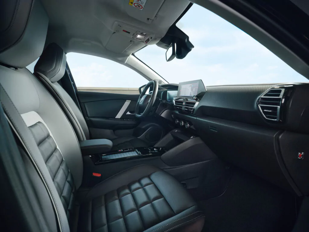 Das Bild zeigt den Innenraum eines modernen Fahrzeugs mit schwarzen, gesteppten Ledersitzen, einem digitalen Armaturenbrett, einem Touchscreen-Display und schlanken, minimalistischen Designdetails. Die Tür auf der Fahrerseite ist geschlossen, und der Innenraum wirkt geräumig und sauber.