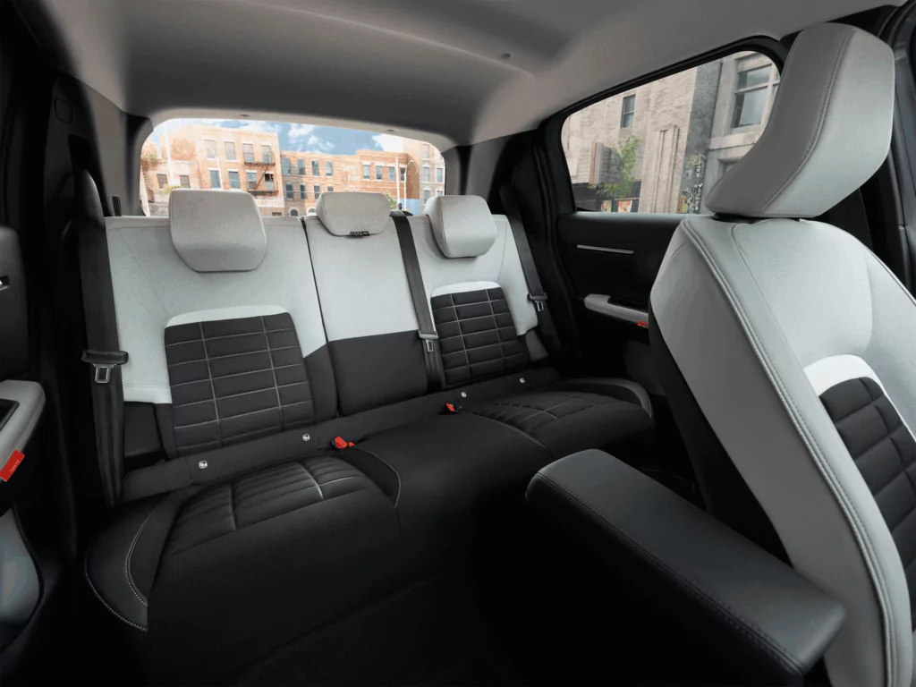 Rückansicht eines Citroen C3 You mit schwarz-weißen Sitzen, einer geräumigen hinteren Reihe mit drei Kopfstützen und großen Fenstern, die eine städtische Straße mit Häusern im Freien zeigen.