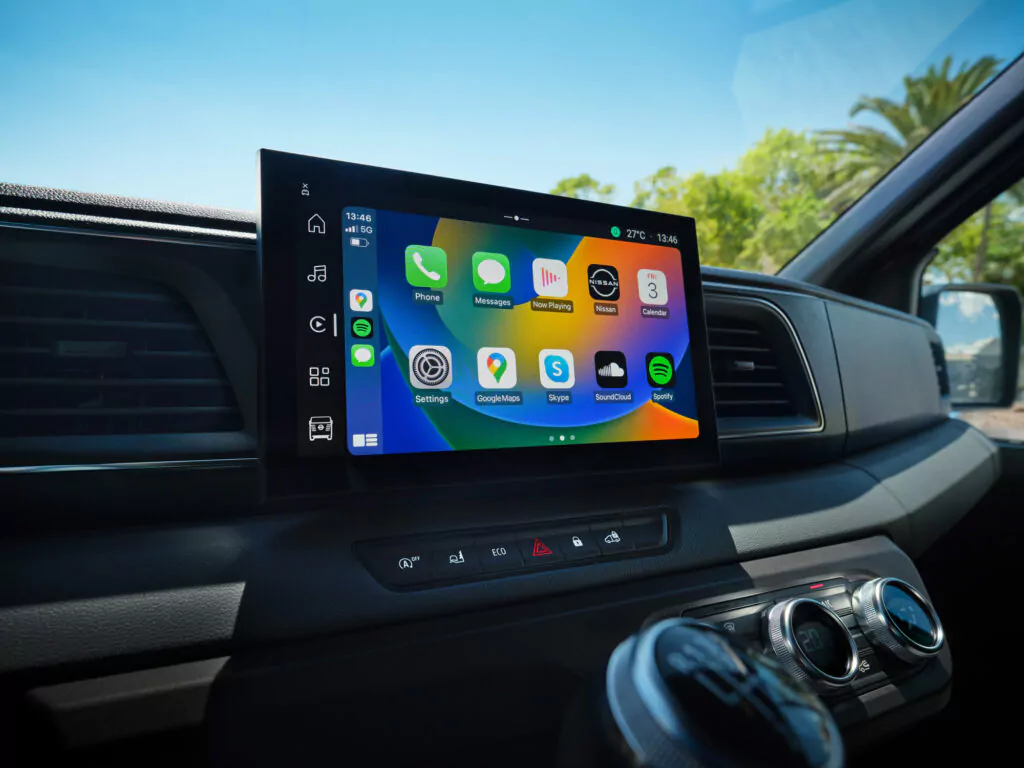 Der Bildschirm des Armaturenbretts eines Autos zeigt eine bunte Oberfläche mit verschiedenen App-Symbolen, darunter Telefon, Nachrichten, Karten, Musik und Wetter - vor einem sonnigen Hintergrund im Freien. Jetzt den Nissan Interstar günstig leasen und moderne Technik erleben.