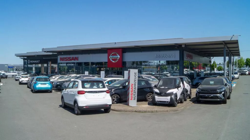 Ein Autohaus in Bielefeld mit den Logos von Nissan, Renault, Dacia und Leapmotor, mit verschiedenen Neu- und Gebrauchtwagen, die an einem sonnigen Tag vor und im Ausstellungsraum geparkt sind.