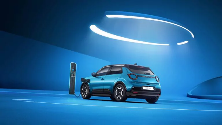 Ein blauer Elektro-SUV parkt und lädt an einer Ladestation in einem modernen, blau beleuchteten Raum mit geschwungenen Leuchten an der Decke.