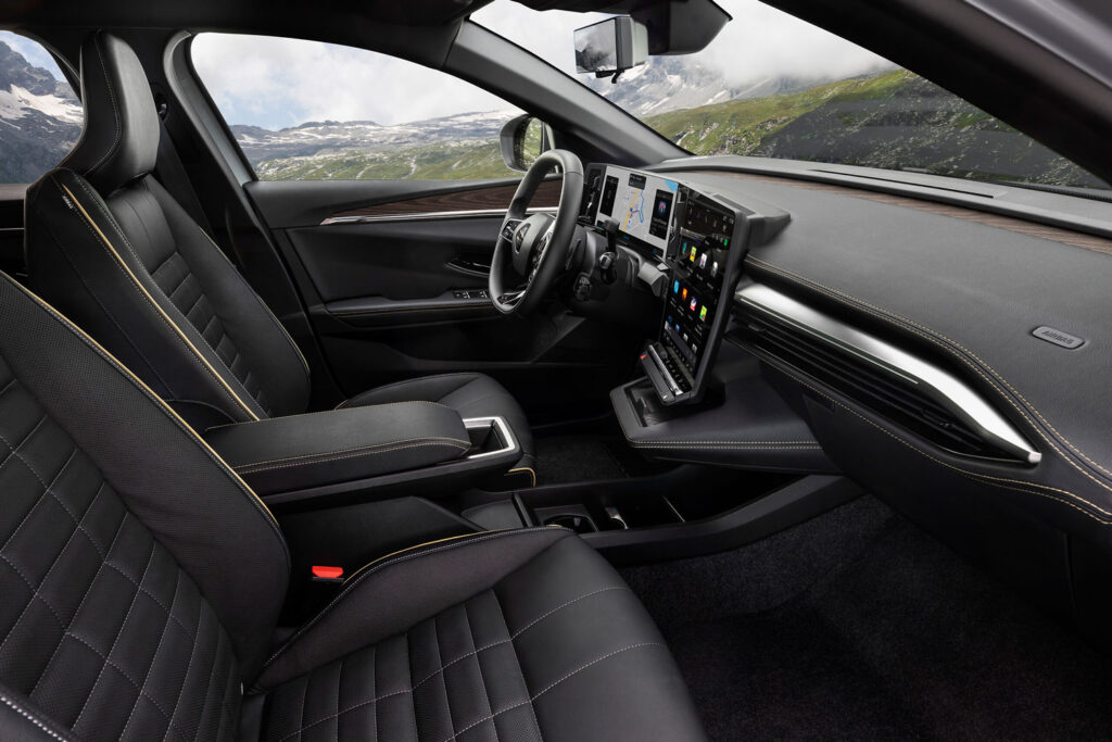 Modernes Interieur mit schwarzen Ledersitzen, gelben Nähten, einem digitalen Armaturenbrett und einem großen zentralen Touchscreen-Display. Durch die Fenster sind Berge und Grünflächen zu sehen.