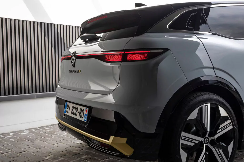 Rückansicht eines auf Kopfsteinpflaster geparkten silbernen Renault SUV mit modernen Rückleuchten, einem Heckspoiler, einem französischen Nummernschild und goldfarbenen Akzenten im Bereich der Stoßstange.