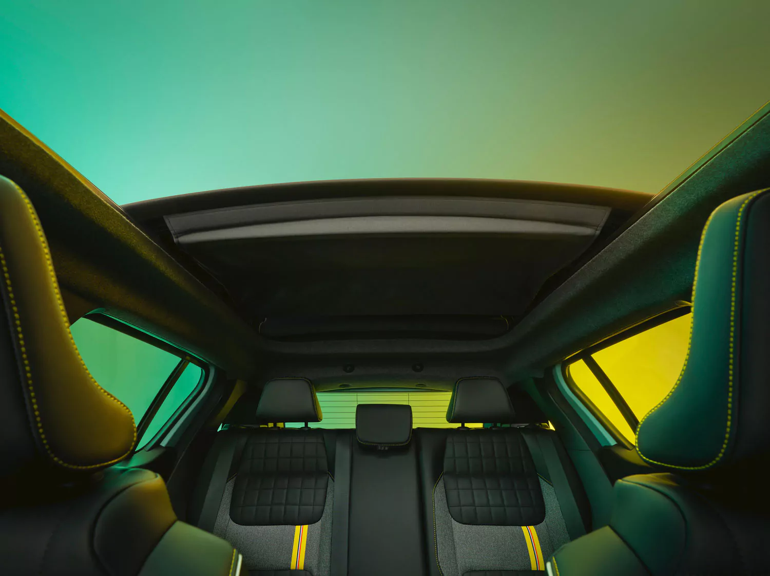 Blick von der Rückbank eines Autos mit schwarzen Ledersitzen und gelben Nähten, mit offenem Schiebedach und einem grün-gelben Himmelsschatten darüber.