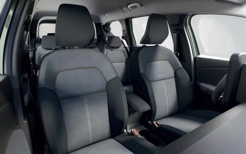 Die Innenansicht eines modernen Dacia Jogger Essential Leasing zeigt die mit dunklem Stoff bezogenen Vorder- und Rücksitze mit hellen Nähten, orangefarbenen Akzenten und dem E2C-Schriftzug auf den Sitzlehnen.
