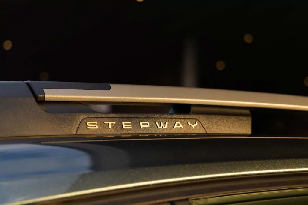 Nahaufnahme einer Dachreling des Dacia Sandero Essential für 89 € mtl. geleast, mit dem Wort STEPWAY auf einem schwarzen Teil, vor einem verschwommenen dunklen Hintergrund mit kleinen Lichtpunkten.