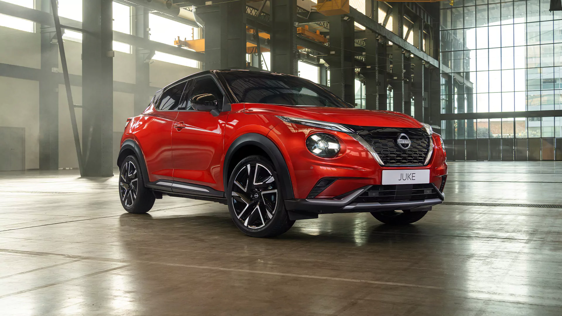 Ein roter Nissan Juke SUV steht in einem geräumigen Gebäude im Industriestil mit großen Fenstern und freiliegenden Stahlträgern, was den Reiz dieses einzigartigen Designs unterstreicht – perfekt für alle, die auf der Suche nach einem erstklassigen Nissan Juke-Angebot sind.