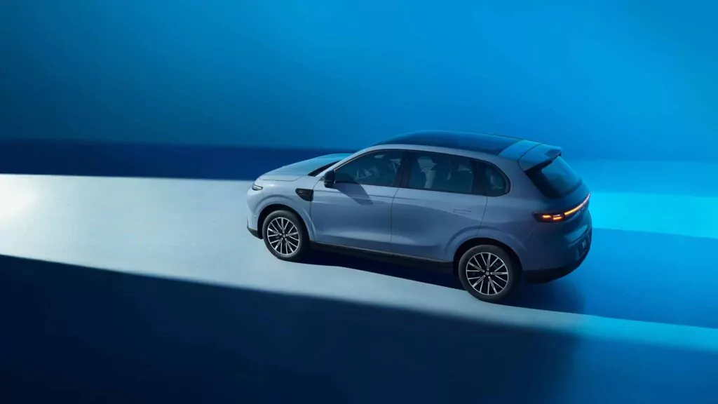 Ein Leapmotor B10 ist auf einer glänzenden Oberfläche geparkt und wird von einem dramatischen Lichtstrahl in einer ansonsten dunkelblauen Umgebung beleuchtet. Das Fahrzeug wird aus einem erhöhten Winkel von der Rückseite aus betrachtet.