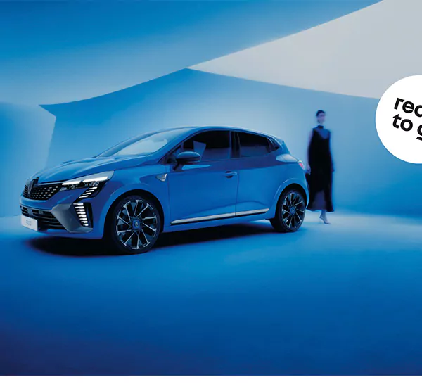 Ein blaues Auto ist in einem modernen, futuristisch blau beleuchteten Raum mit geometrischen Deckenformen geparkt. Eine verschwommene Figur steht im Hintergrund. Ein weißer kreisförmiger Text auf der rechten Seite lautet: "Ready to go".