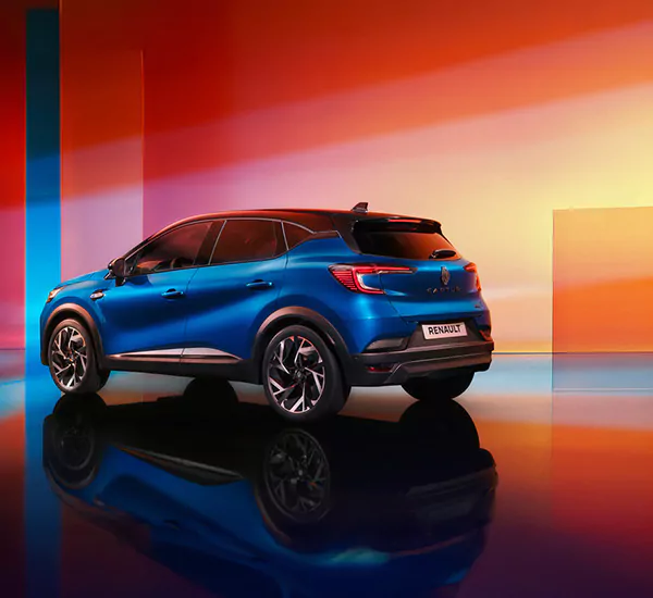 Ein blauer Renault SUV wird in einem farbenfrohen, modernen Studio mit roter, oranger und blauer Beleuchtung ausgestellt. Das Heck und die Seite des Fahrzeugs sind sichtbar, und sein Spiegelbild erscheint auf dem glänzenden Boden.