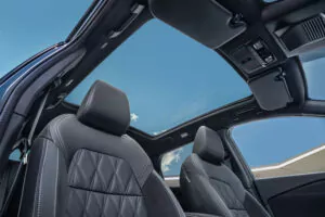 Blick aus dem Innenraum eines Nissan Qashqai N-Connecta mit schwarzen Ledersitzen mit weißen Nähten und einem großen Panorama-Schiebedach, das einen klaren blauen Himmel mit ein paar Wolken zeigt.