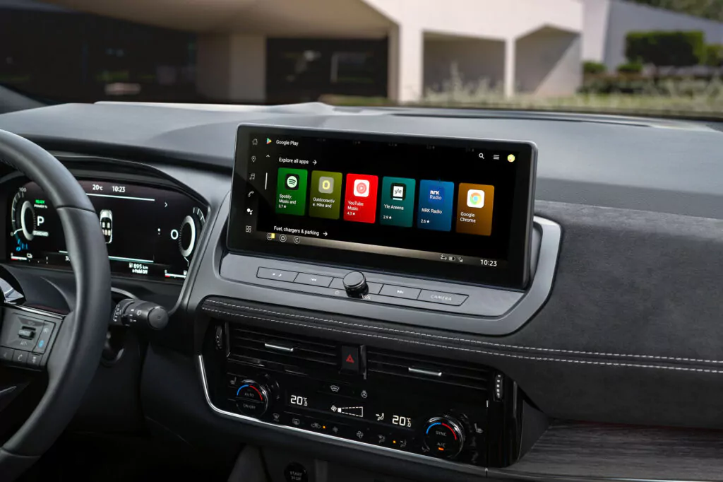 Nahaufnahme eines Nissan Qashqai N-Connecta Armaturenbretts mit einem großen Touchscreen mit App-Symbolen, Klimabedienelementen darunter und einem Teil des Lenkrads. Der Innenraum besticht durch sein modernes und schlankes Design.