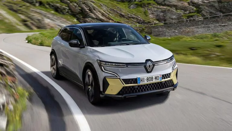 Ein weißer Renault Megane E-Tech Leasing Elektro-Geländewagen mit gelben Akzenten fährt eine kurvenreiche Bergstraße entlang, die von Grünflächen und felsigen Hängen umgeben ist.
