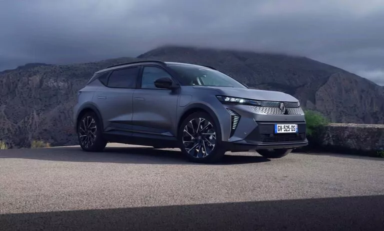 Ein schnittiger, mattgrauer Geländewagen - perfekt für das Renault Scenic-Leasing - parkt auf einer malerischen Bergstraße unter einem wolkenverhangenen Himmel, mit schroffen Felsen und grüner Landschaft im Hintergrund.