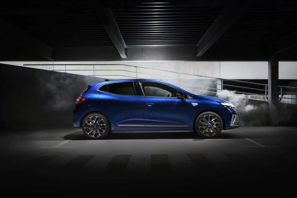 Ein blauer Renault Clio mit Fließheck steht in einer schwach beleuchteten Garage mit grauen Betonwänden und einer Rampe dahinter. Rauch oder Nebel umgibt das Heck des Fahrzeugs und erzeugt einen dramatischen Effekt - perfekt, um die Leasingoptionen für den Renault Clio zu präsentieren.
