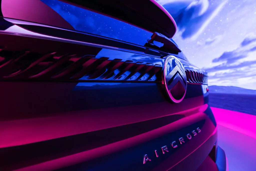 Nahaufnahme des Hecks eines Citroen e-C3 Aircross, hervorgehoben durch dramatische rosa und blaue Beleuchtung, vor einem Nachthimmel voller Sterne und Wolken.