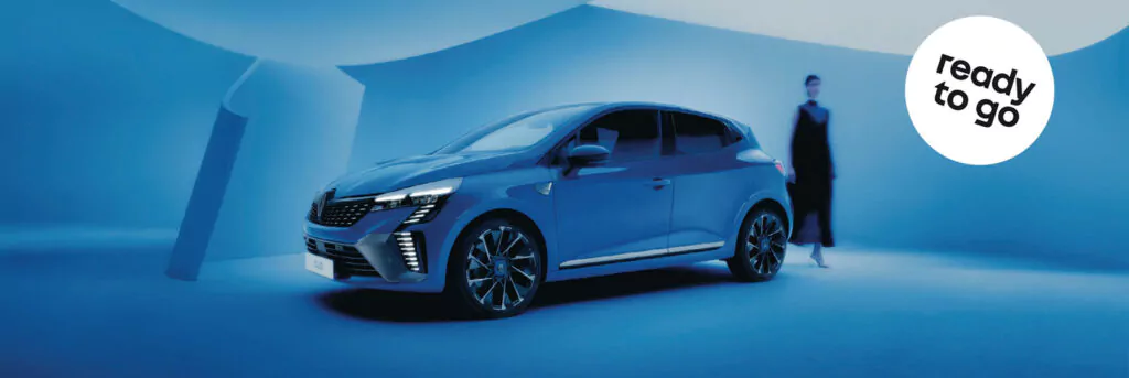 Ein blaues Auto ist in einem modernen, blau beleuchteten Raum geparkt. Eine dunkel gekleidete Person steht in der Nähe. In der oberen rechten Ecke ist ein weißer Kreis mit der Aufschrift "ready to go" zu sehen.