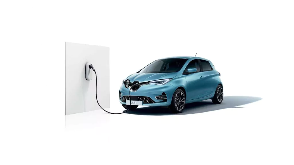 Ein blaues Elektroauto ist an eine weiße Ladestation angeschlossen, wobei das Kabel an der Vorderseite des Autos angeschlossen ist.