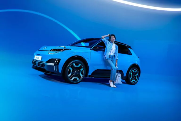 Eine Person in Freizeitkleidung lehnt an einem blauen modernen Geländewagen in einem hell erleuchteten, futuristischen blauen Raum mit gekrümmten Lichtstreifen im Hintergrund.