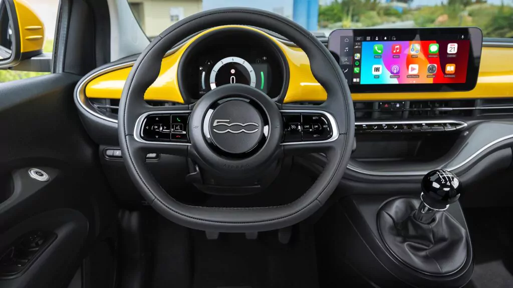 Der Innenraum eines Fiat 500 mit Lenkrad, digitalem Kombiinstrument, manuellem Schaltknüppel und einem Armaturenbrett mit Touchscreen-Display, das Smartphone-Apps unterstützt.
