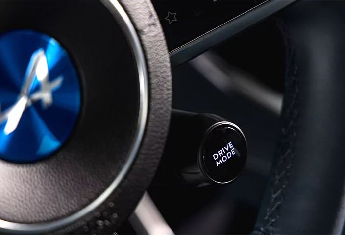 Nahaufnahme eines Alpine A390-Lenkrads mit einer runden Fahrmodus-Taste und einem blauen Emblem in der Mitte.