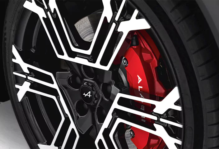 Schwarz-weiße Leichtmetallfelge an einem Alpine A390, mit rotem Bremssattel und dem Alpine-Logo auf der Radkappe.