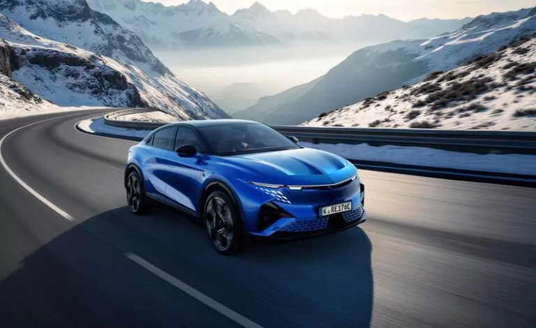 Ein Alpine A390 fährt auf einer kurvenreichen Bergstraße mit schneebedeckten Gipfeln und Hängen im Hintergrund unter einem klaren Himmel.