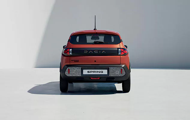 Ein rotes Dacia Spring-Elektroauto wird von hinten gezeigt, geparkt auf einer glatten weißen Fläche mit einem einfarbig weißen Hintergrund. Der Schriftzug des Autos und das SPRING-Kennzeichen sind sichtbar.