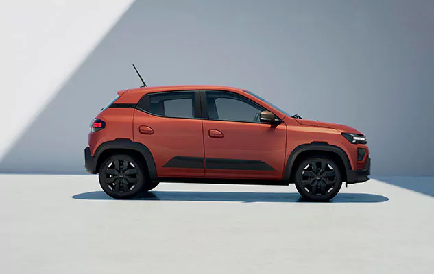 Seitenansicht eines orangefarbenen kompakten Geländewagens, der auf einer sauberen, hellgrauen Fläche mit einem geometrischen Schattenmuster an der Wand dahinter geparkt ist.