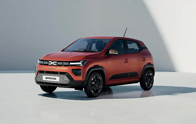 Ein roter kompakter Geländewagen parkt auf einer glatten, hellen Fläche vor einer schlichten, weißen Wand. Der Wagen hat schwarze Räder, moderne Scheinwerfer und einen Kühlergrill mit dem Logo DC. Auf dem Nummernschild steht SPRING.